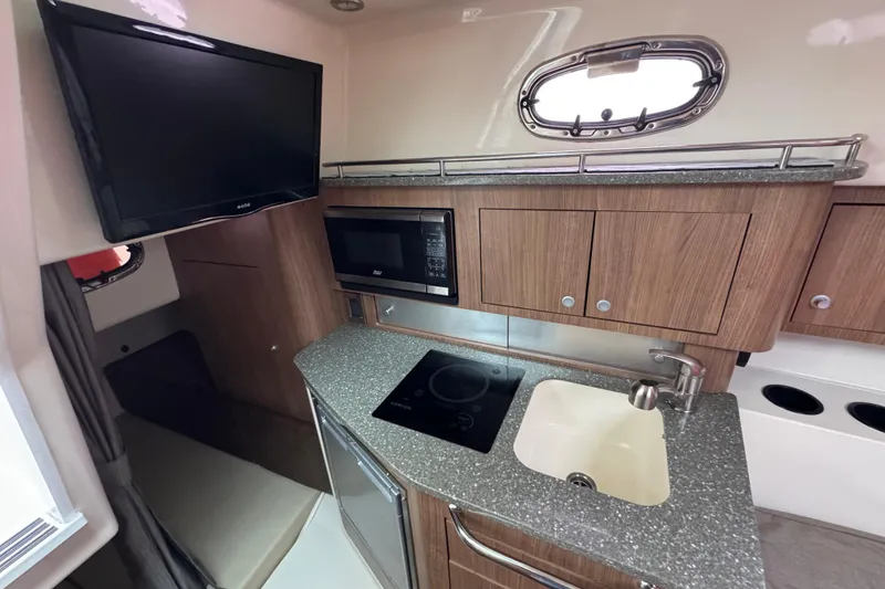 Slide: The Image of 2016 Boston Whaler 315 Conquest interior kitchen with TV, microwave, sink, and stove. - 35