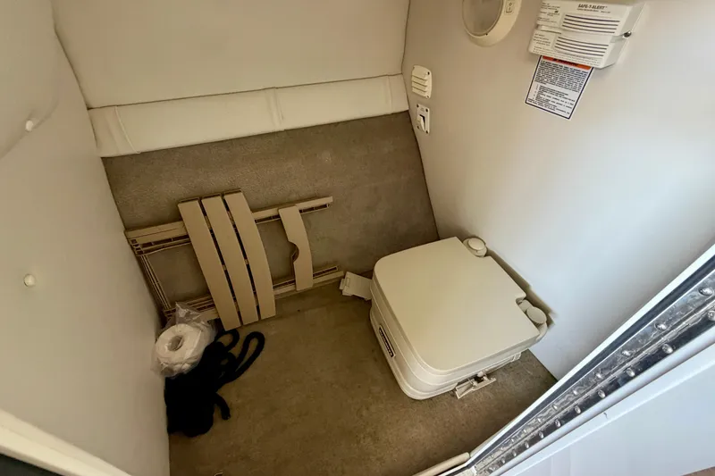 Slide: The Image of Interior of a 2006 Crownline 266 BR boat featuring a compact portable toilet. - 21
