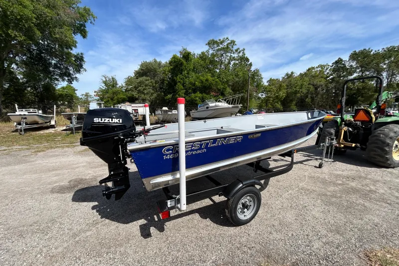 Slide: The Image of 2026 Crestliner 1469 Outreach boat with Suzuki motor on trailer, parked outdoors. - 4