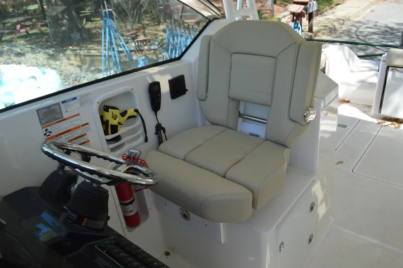 Slide: The Image of 2018 Pursuit DC 295 Dual Console boat interior with steering wheel and beige captain's seat. - 11
