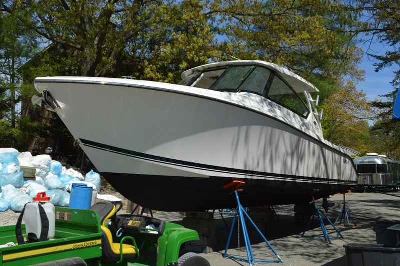 Slide: The Image of 2018 Pursuit DC 295 Dual Console boat on stands, surrounded by trees and equipment. - 2