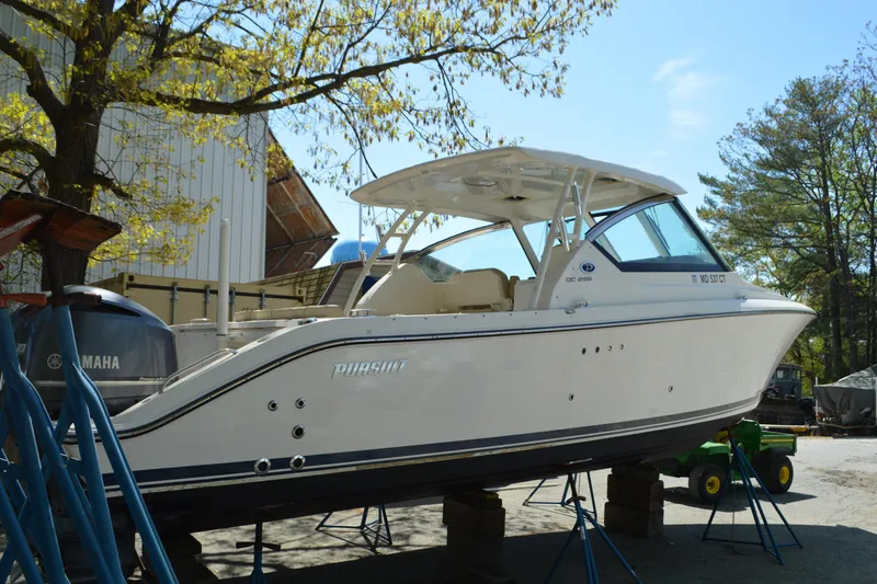 Slide: The Image of 2018 Pursuit DC 295 Dual Console boat on stands, outdoors near trees and building. - 5