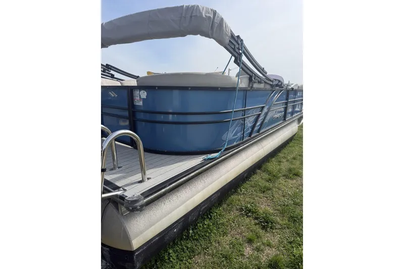 Slide: The Image of 2018 Starcraft SLS 3 pontoon boat with blue exterior, docked on grass. - 2