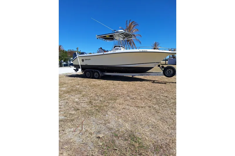 The Image of 2004 Century 2600 Center Console boat on trailer, parked on grass under clear blue sky. - 1