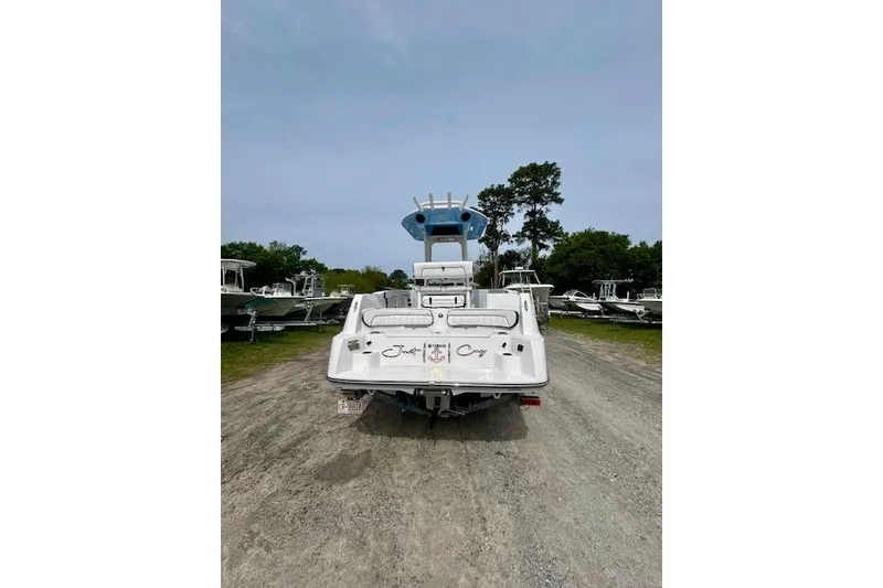 Slide: The Image of 2024 Yamaha Boats 222 FSH Sport E, rear view, parked on gravel with trees in background. - 14