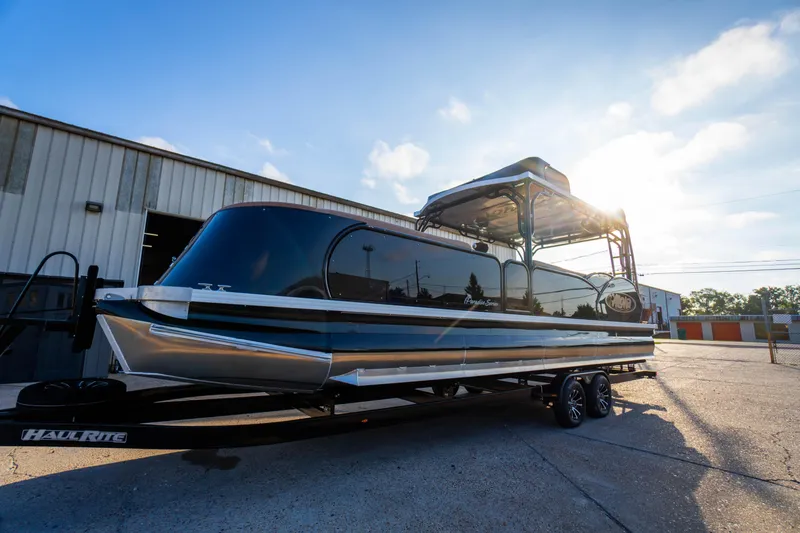 Slide: The Image of 2026 Aloha Paradise 300 Sundeck boat on trailer, parked outdoors under a bright sky. - 12