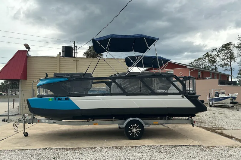 Slide: The Image of 2023 Sea-Doo Switch 19 pontoon boat on trailer, parked outdoors under cloudy sky. - 2