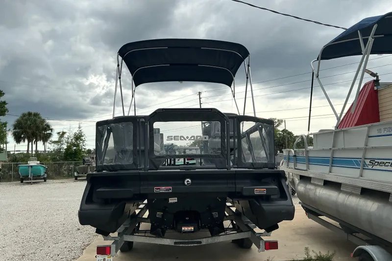 Slide: The Image of 2023 Sea-Doo Switch 19 pontoon boat with canopy, parked on a trailer under cloudy skies. - 4