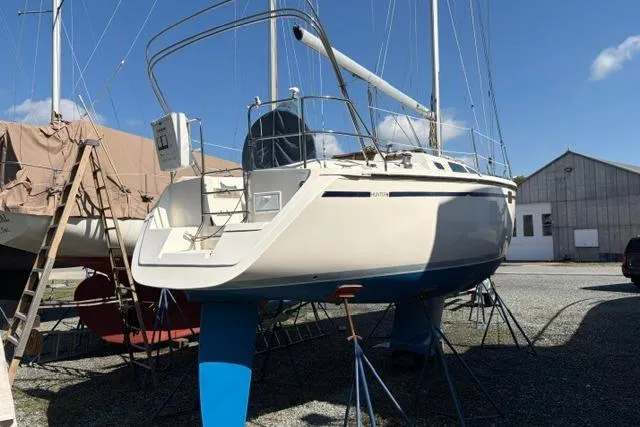 Slide: The Image of 1990 Hunter 33.5 sailboat on stands, in a boatyard under clear blue sky. - 3