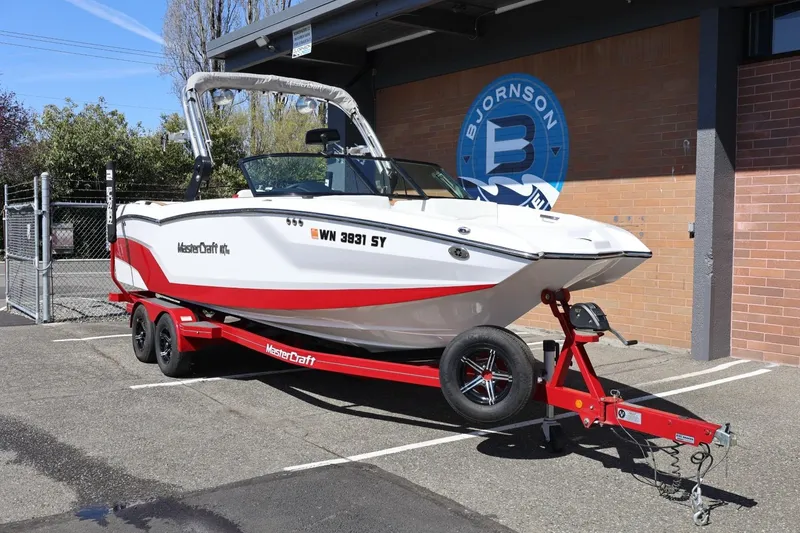Slide: The Image of 2021 MasterCraft NXT24 boat on trailer, parked outdoors near a brick building. - 3