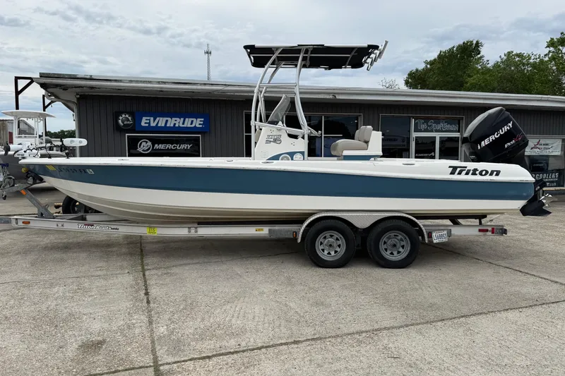 The Image of 2010 Triton 240 LTS Pro boat on trailer, parked outside dealership with Evinrude and Mercury signage. - 1