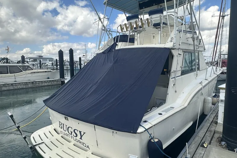 Slide: The Image of 1981 Hatteras 43 Convertible yacht docked with blue cover, labeled "Bugsy" in Stuart, Florida. - 2