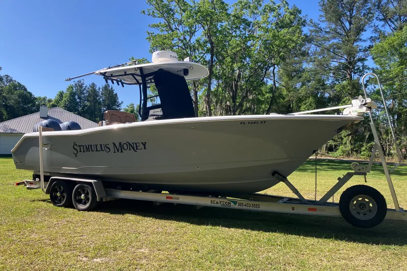 The Image of 2020 Sea Hunt Gamefish 27 boat on trailer, labeled "Stimulus Money," parked on grass. - 0