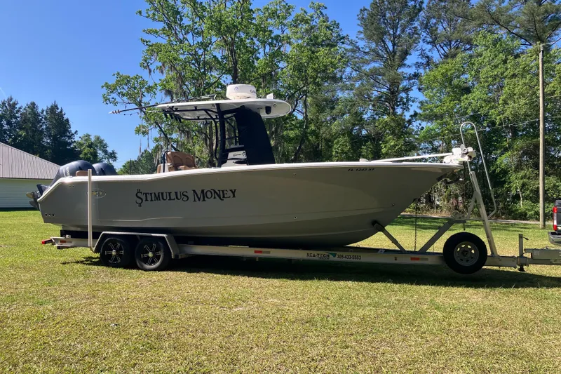 Slide: The Image of 2020 Sea Hunt Gamefish 27 boat on trailer, labeled "Stimulus Money," parked on grass. - 94
