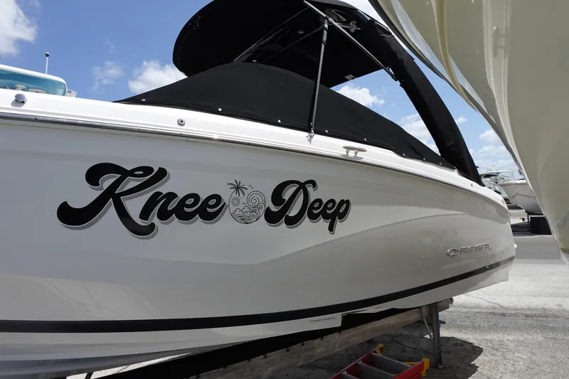 The Image of 2021 Regal 23 OBX boat named "Knee Deep" with black canopy, docked under blue sky. - 0