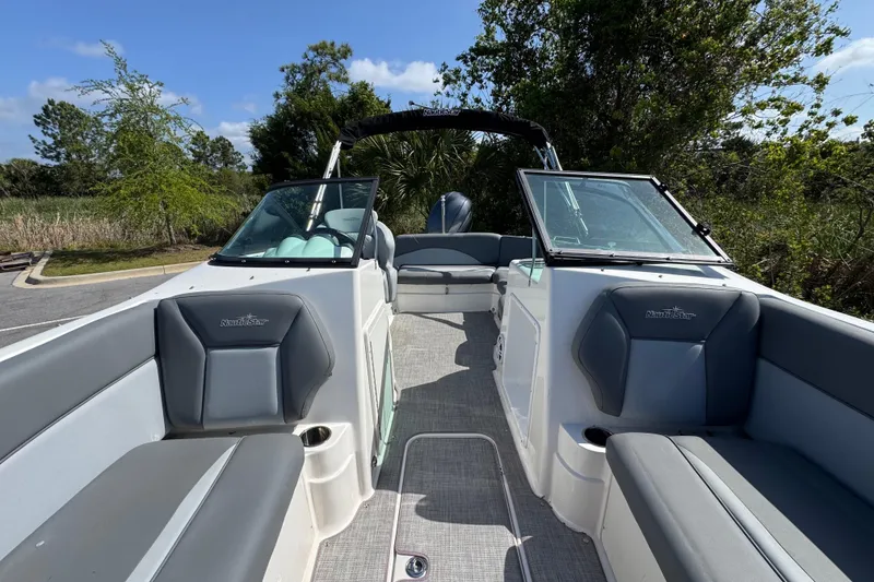 Slide: The Image of 2023 NauticStar 243 DC boat interior with gray seating and open deck, surrounded by greenery. - 10