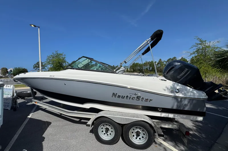 Slide: The Image of 2023 NauticStar 243 DC boat on trailer, parked outdoors under clear blue sky. - 6