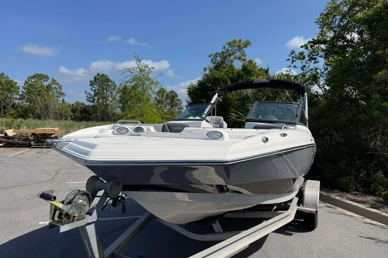 Slide: The Image of 2023 NauticStar 243 DC boat on trailer, parked outdoors with trees in background. - 7