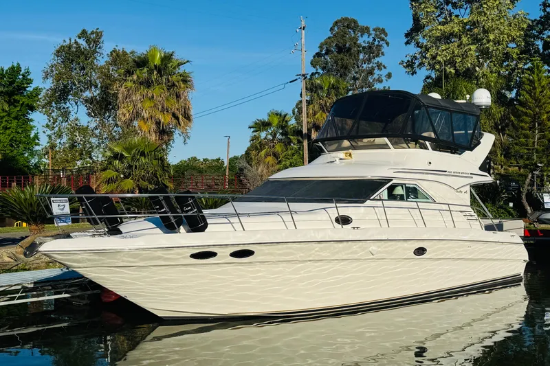 The Image of 2000 Sea Ray 400 Sedan Bridge yacht docked, surrounded by lush greenery and calm waters. - 0