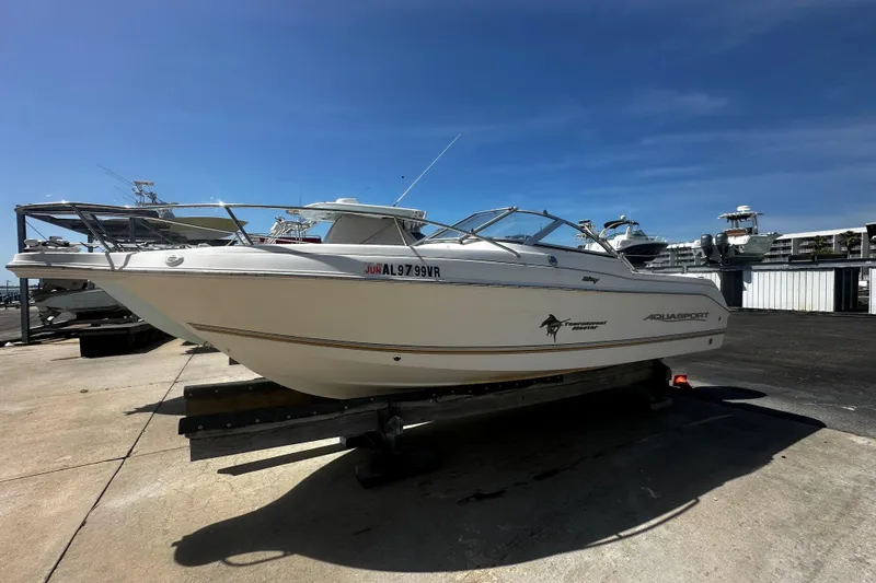The Image of 2004 Aquasport 215 Osprey Sport boat on a trailer under clear blue sky. - 1