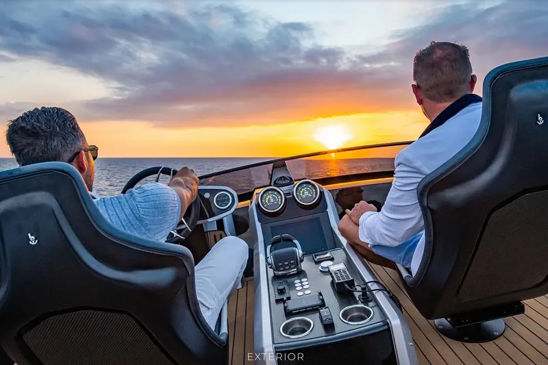Slide: The Image of 2023 Sunseeker 65 Sport Yacht cruising at sunset with two people at the helm. - 66