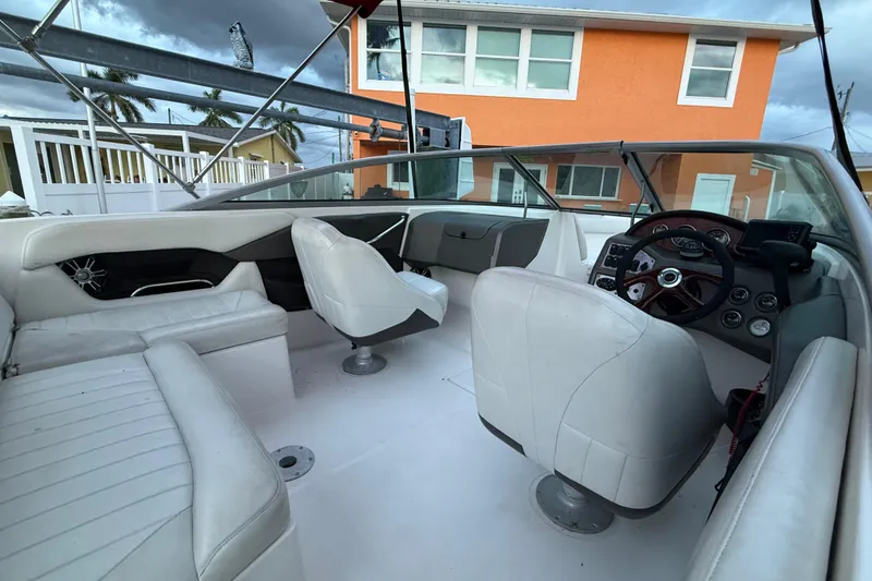 Slide: The Image of 2004 Regal 2000 Bowrider interior with white seating and dashboard, near orange house. - 32