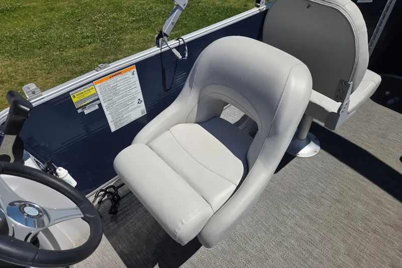 Slide: The Image of Captain's seat on 2021 Godfrey Sweetwater 1880 FX boat, featuring steering wheel and safety labels. - 11