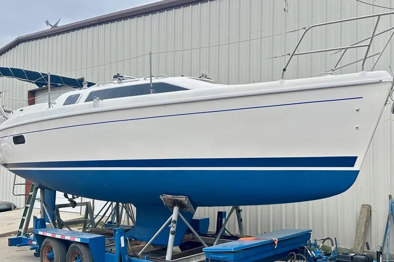 The Image of 1996 Hunter Marine 280 sailboat on trailer, white and blue hull, docked near a building. - 1