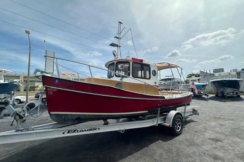 The Image of 2015 Ranger Tugs R-21 EC boat on trailer, vibrant red hull, parked outdoors. - 0