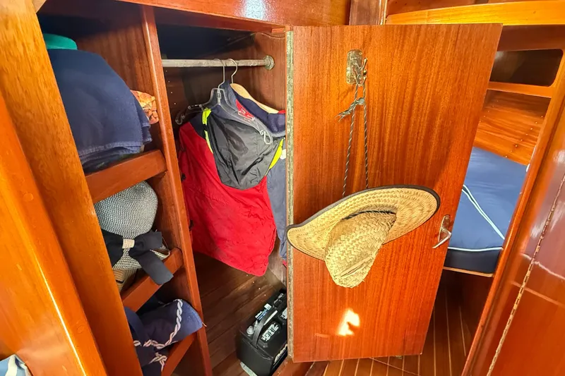 Slide: The Image of Wooden closet interior on a 1986 Vindo 45 sailboat, with clothes and a straw hat. - 46