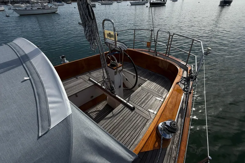 Slide: The Image of Sailboat cockpit of 1986 Vindo 45, featuring wooden deck and steering wheel, docked in marina. - 48