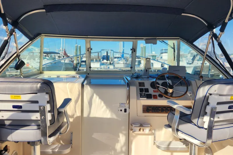 Slide: The Image of 2003 Mainship Pilot 30-II boat cockpit with steering wheel and dual seats, docked at marina. - 23