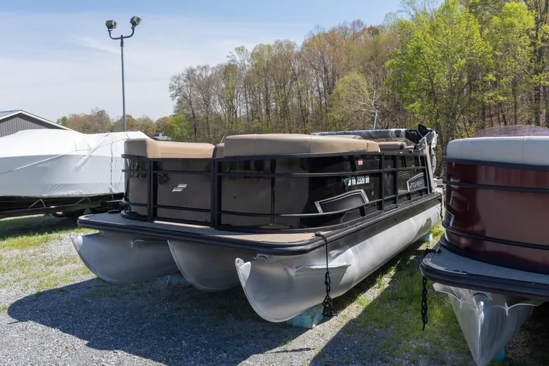 Slide: The Image of 2025 Starcraft EXS 3 pontoon boat parked outdoors on gravel, surrounded by trees. - 3