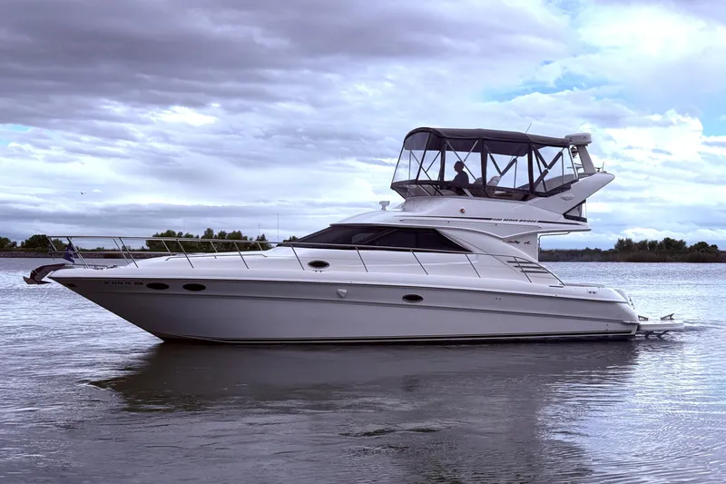 The Image of 1999 Sea Ray 400 Sedan Bridge yacht cruising on a calm lake under cloudy skies. - 0