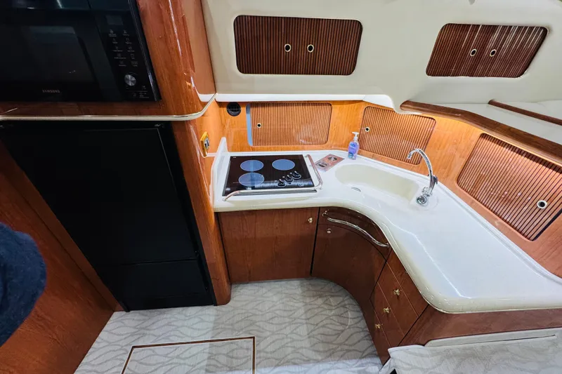 Slide: The Image of 1999 Sea Ray 400 Sedan Bridge kitchen with stove, sink, and wooden cabinetry. - 71