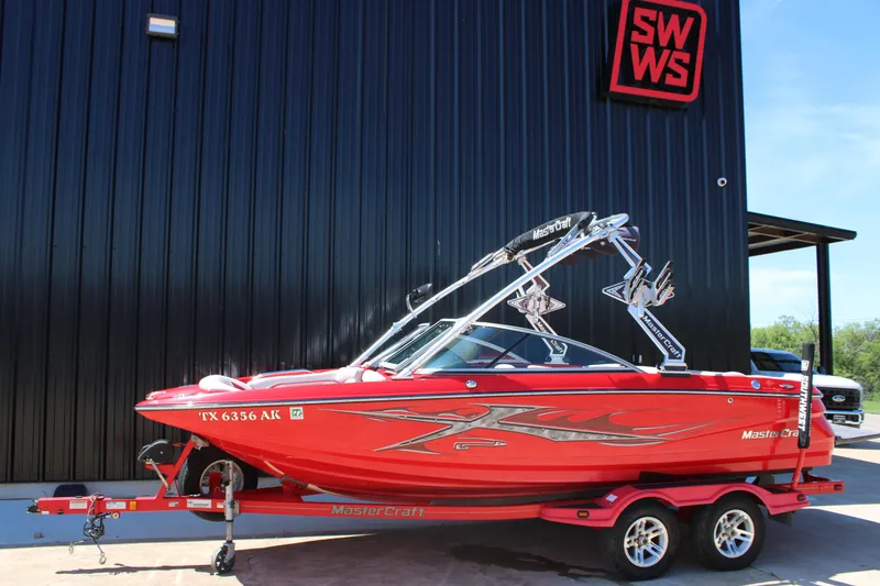 The Image of Red 2007 MasterCraft X2 boat on trailer, parked outside a black building. - 0