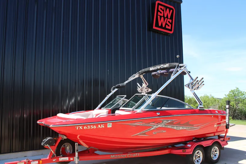 Slide: The Image of 2007 MasterCraft X2 boat in vibrant red on a trailer, parked outside a building. - 2