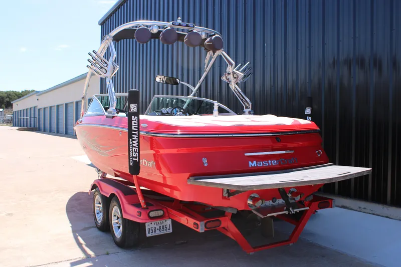 Slide: The Image of Red 2007 MasterCraft X2 boat on trailer, parked near storage units. - 6