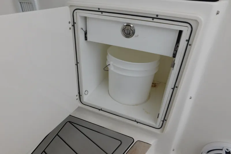 Slide: The Image of Storage compartment with a white bucket on a 2023 Pursuit OS 325 Offshore boat. - 25
