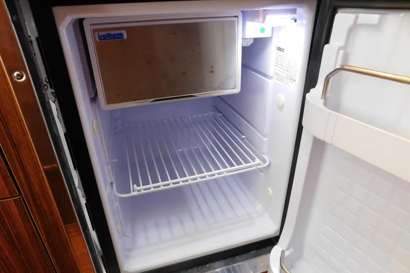 Slide: The Image of Open refrigerator inside 2023 Pursuit OS 325 Offshore boat, featuring wire shelf and freezer compartment. - 52