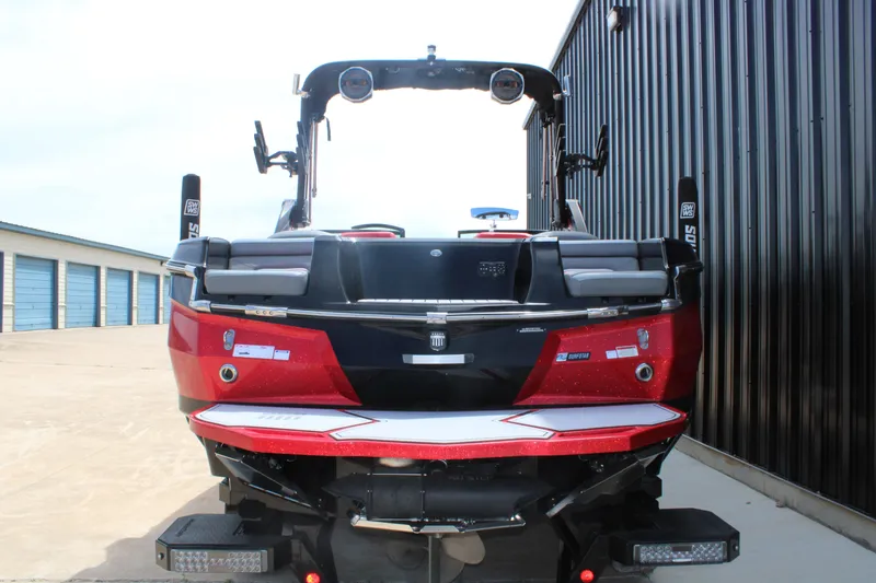 Slide: The Image of 2024 MasterCraft XStar S boat, rear view, red and black design, parked near storage units. - 17