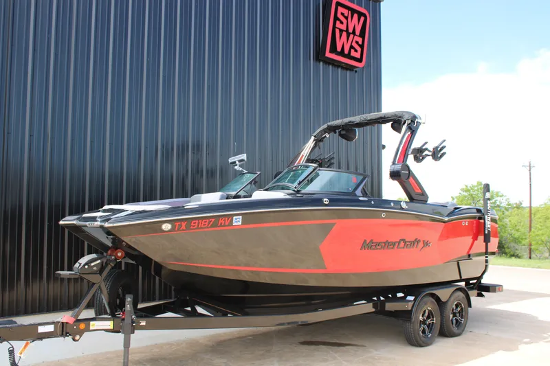 Slide: The Image of 2024 MasterCraft XStar S boat on trailer, parked outside a building. - 2