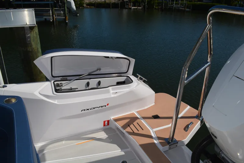 Slide: The Image of 2025 Axopar 29 Sun-Top boat with open storage compartment, docked by the water. - 5