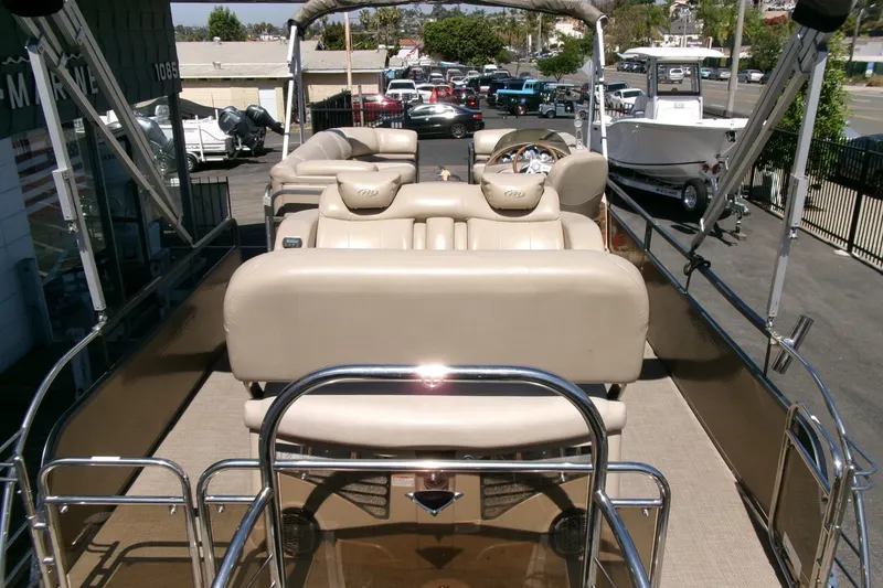 Slide: The Image of 2015 Manitou 25 SES Flip pontoon boat with beige seating and steering wheel, parked outdoors. - 33