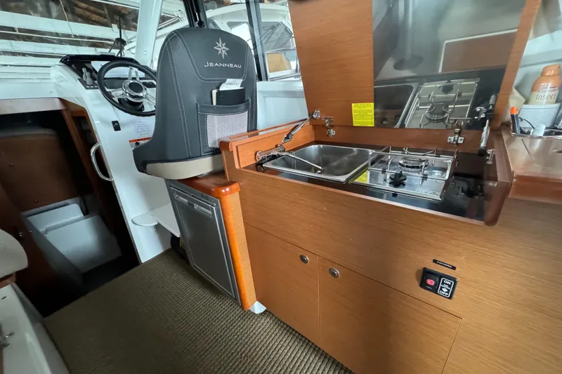 Slide: The Image of Interior of 2016 Jeanneau Merry Fisher 855 showing helm and compact kitchen area. - 13