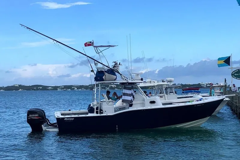 The Image of 1998 Mirage Sportfish boat docked, featuring Suzuki outboard motor, flags, and scenic coastal backdrop. - 0