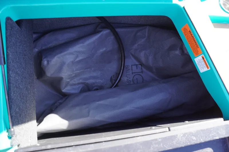 Slide: The Image of Ballast bag inside 2023 Axis T235 boat compartment, featuring warning labels and teal interior. - 29
