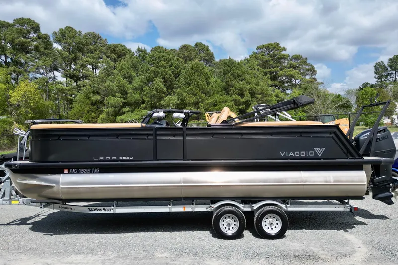 Slide: The Image of 2025 Viaggio Lago X-U 24 pontoon boat on trailer, surrounded by trees and cloudy sky. - 1
