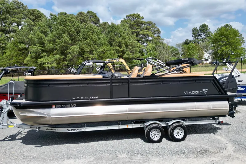 Slide: The Image of 2025 Viaggio Lago X-U 24 pontoon boat on trailer, surrounded by trees and other boats. - 2