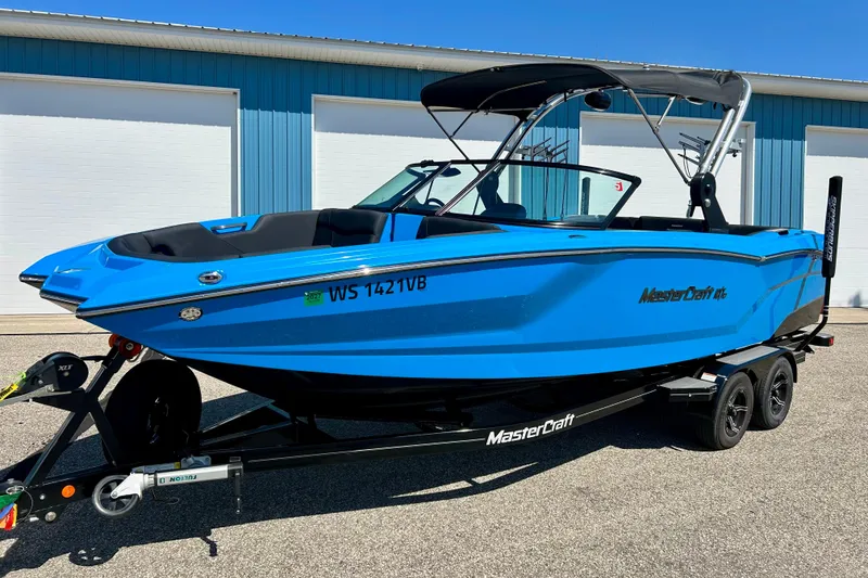 The Image of 2021 MasterCraft NXT24 boat in vibrant blue, parked on a trailer outside a blue building. - 0